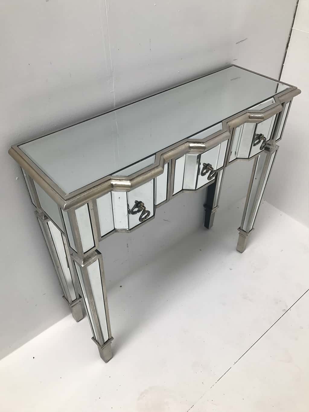 Charleston mirrored console table with 3 drawers, silver wood edging, glass top, tapered legs and drop Ring brass pulls